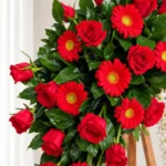 Detalle de la Corona Fúnebre Eternidad: rosas rojas y gerberas rojas entre follaje verde.