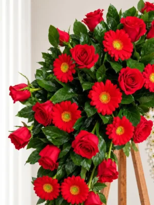 Detalle de la Corona Fúnebre Eternidad: rosas rojas y gerberas rojas entre follaje verde.
