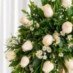 Detalle de la Corona Fúnebre Luz Eterna: rosas crema, margaritas blancas y gypsophila entre follaje verde.