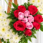Detalle de la Corona Fúnebre Ternura: ramillete de rosas rojas con rosas rosadas al centro y helecho, sobre el corazón de crisantemos blancos.