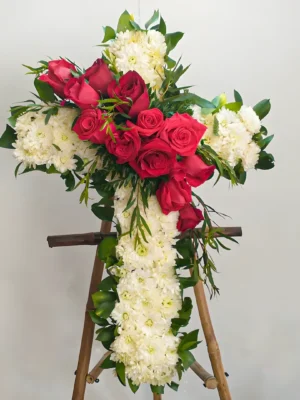 Arreglo fúnebre en forma de cruz con rosas rojas en cascada y crisantemos blancos, sobre atril de madera