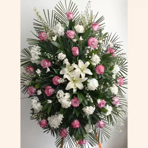 Pedestal fúnebre en forma de abanico con hojas de palma, rosas fucsia, hortensia y lirios blancos, cinta naranja.