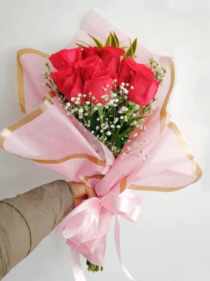 Bouquet de Flores Centella con rosas rojas y gypsophila, en papel rosado con borde dorado y moño rosado.