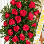 Detalle de la Corona Fúnebre Aurora: rosas rojas entre helecho, con la cinta blanca de dedicatoria en letras doradas.