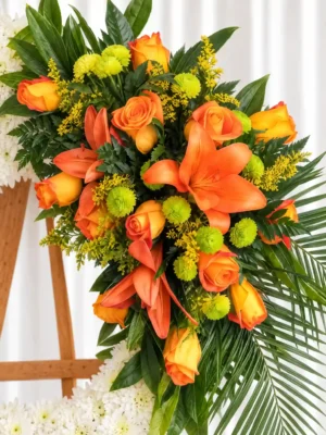 Detalle de la Corona Fúnebre Descansa en Paz: rosas y lirios naranjas, pompones verdes y solidago amarillo entre hojas de palma.
