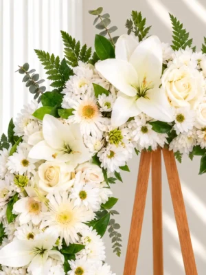 Detalle de la Corona Fúnebre Esmeralda: lirios blancos, rosas crema, gerberas y margaritas blancas con helecho y eucalipto.