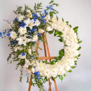 Corona de flores blancas azules celestiales ramas naturales follaje verde atril