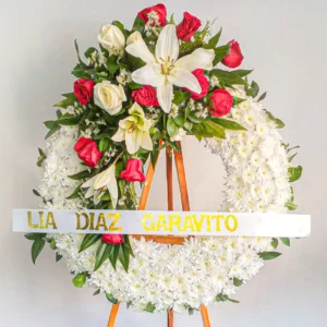 Corona de flores blancas lirios rosas rojas follaje verde atril madera