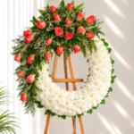 Corona Fúnebre Memoria circular de crisantemos blancos con media corona de rosas coral, caspia y follaje, sobre atril de madera.