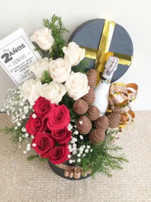 Ramo con rosas rojas y blancas, gypsophila, fresas con chocolate y vino en caja redonda negra decorada con detalles dorados.