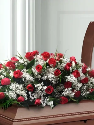 Cubre cofre alargado con rosas rojas y flores blancas pequeñas sobre ataúd de madera