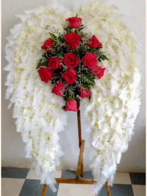 Arreglo fúnebre en forma de alas de ángel con plumas y pompón blanco, y rosas rojas en el centro