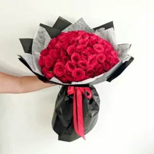 Ramo Buchón con 100 rosas rojas premium, envuelto en papel negro mate con lazo rojo, ideal para ocasiones románticas especiales.