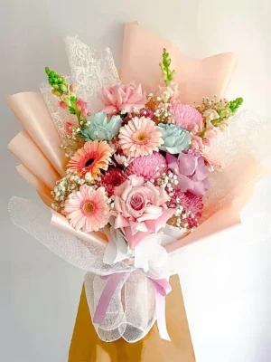 Bouquet de Flores Escarlata en tonos pastel con rosas rosadas, gerberas, crisantemos y gypsophila, en papel durazno.