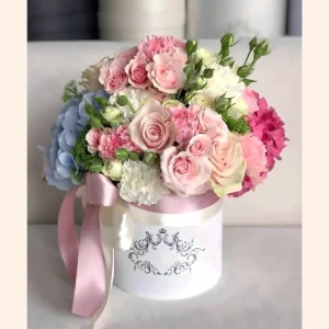 Rosas y claveles rosados con hortensia azul y flores blancas en caja redonda blanca, lazo de raso rosa.
