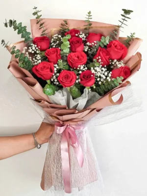 Bouquet de Flores Étincelle con rosas rojas, gypsophila y eucalipto, en papel rosa palo con lazo rosado.