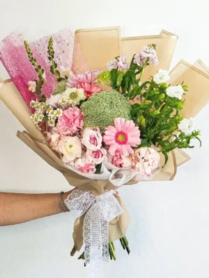 Bouquet de Flores Fleurir con gerberas rosadas, rosas, margaritas y un pompón verde, en papel beige con lazo de encaje.