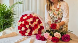 Florista con delantal floreado arreglando rosas rojas y blancas junto a un bouquet grande sobre la mesa.