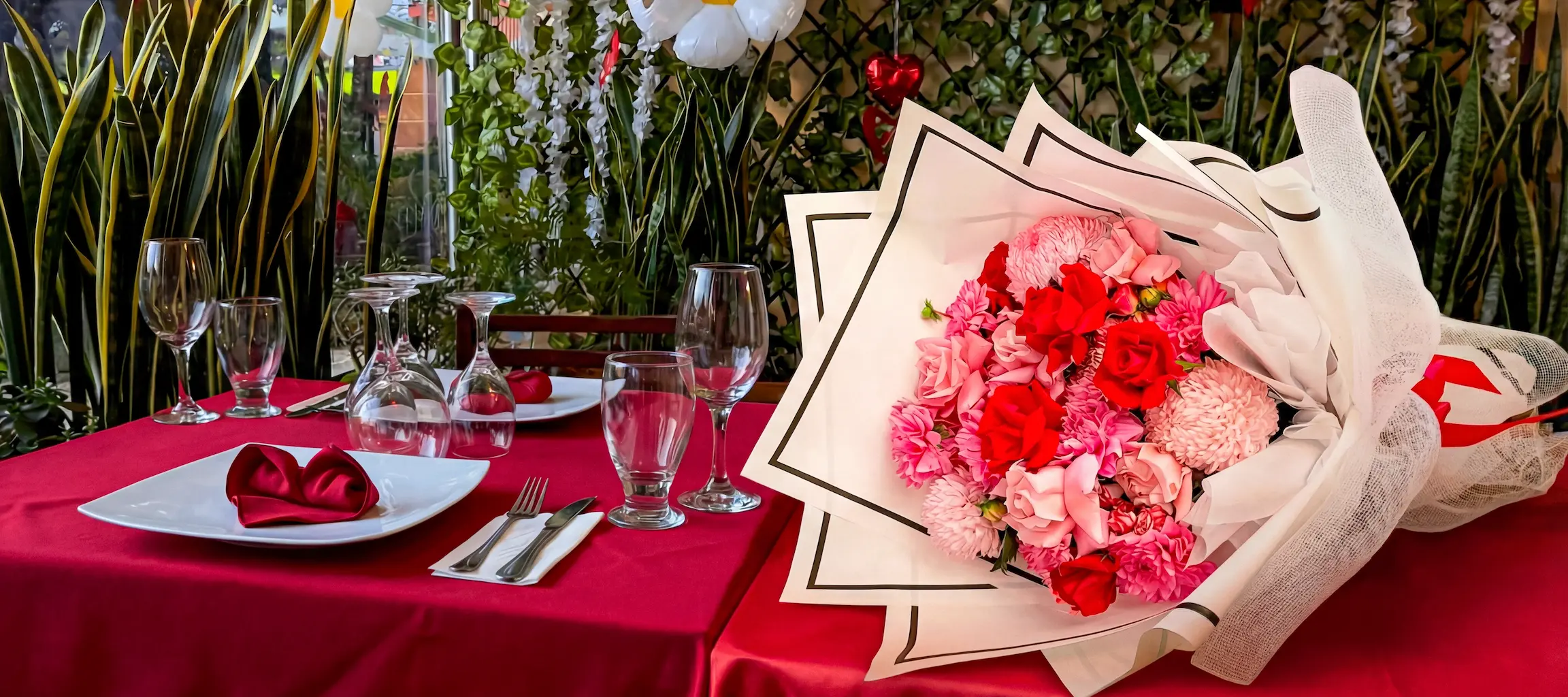 Flores para ocasiones especiales en Bogotá Bouquet de rosas rojas y claveles rosados envuelto en papel elegante sobre mesa de cena romántica de aniversario