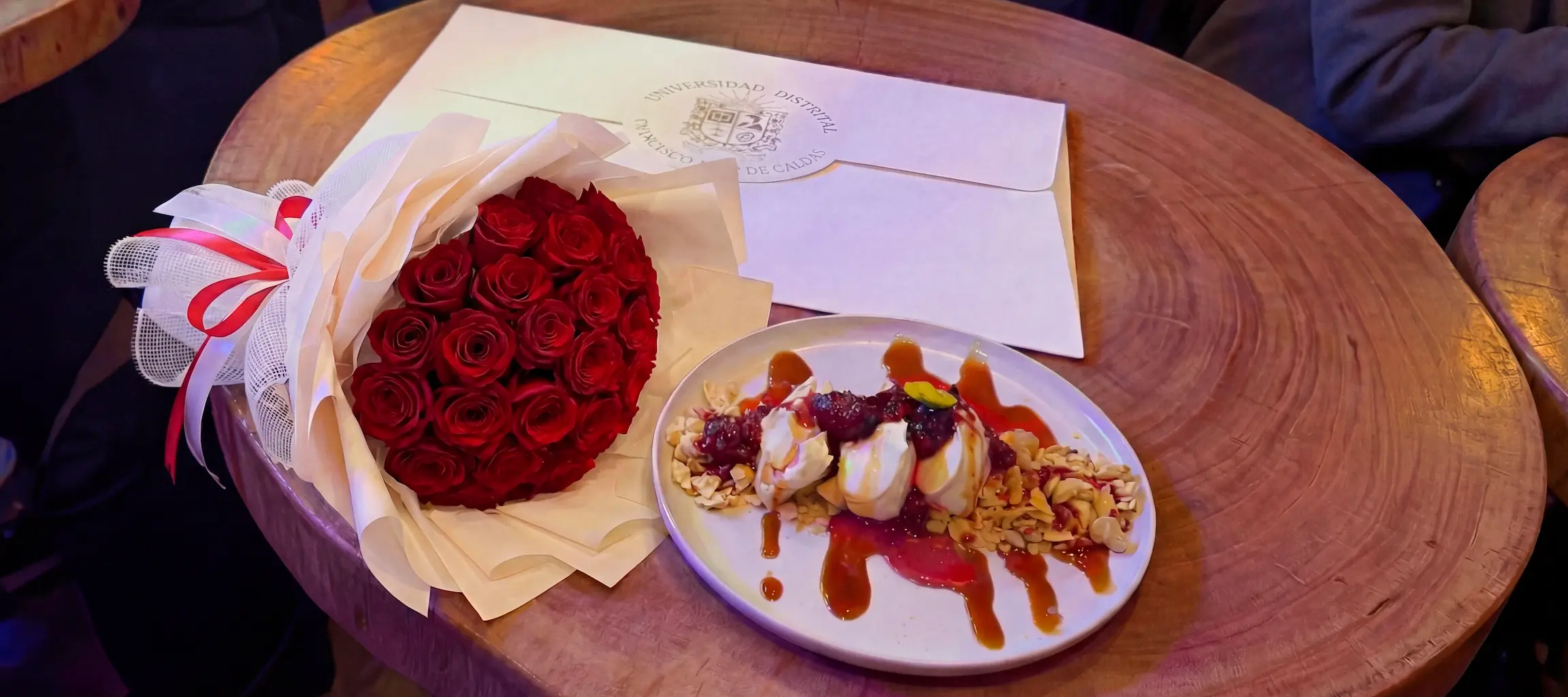 Regalo floral para celebrar momentos Ramo de rosas rojas de graduación envuelto en papel beige junto a postre en restaurante