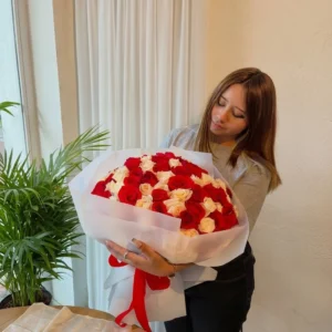Mujer abrazando un gran bouquet de rosas rojas y blancas envuelto en papel blanco con lazo rojo